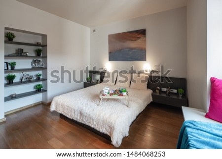 Light bedroom. Shelves with decorative elements. King-size bed. An artwork was createn by photographer in post-production process.