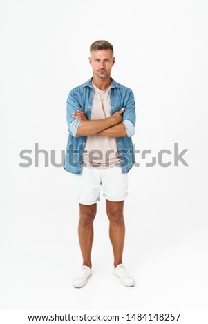 Full length photo of masculine guy in denim shirt keeping arms crossed and looking at you isolated over white background