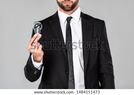 partial view of successful businessman in black suit holding light bulb isolated on grey