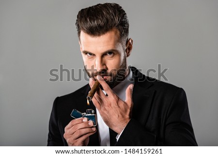 businessman in black suit lighting up cigar isolated on grey