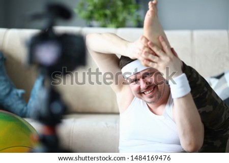 Smiling Man Recording on Camera Leg Stretching. Beard Vlogger Shooting Aerobic Exercise on Digital Camcorder for Sport Vlog. Happy Sportsman Practice Gymnastics in Apartment. Healthy Lifestyle Photo