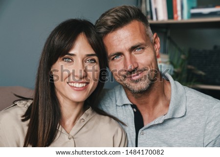 Photo of adult caucasian couple man and woman smiling while cuddling on sofa at home