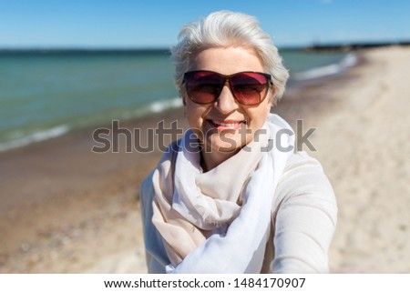 old people and leisure concept - happy smiling senior woman in sunglasses taking selfie on beach in estonia