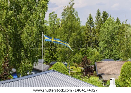 View of swedish flag on top of roof. Green forest trees and blue sky on background. Sweden. Europe.