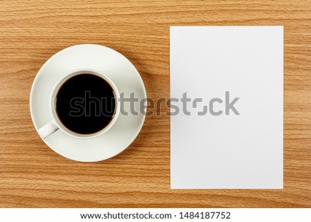 blank note paper and a white coffee cup on wooden desk. - blank space for advertising text.