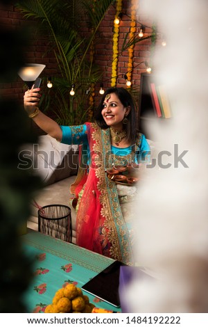 Indian girl holding diwali diya in traditional wear, clicking selfie picture or speaking over smartphone. 