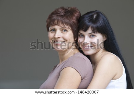 Closeup of a smiling young woman with her mother against gray background