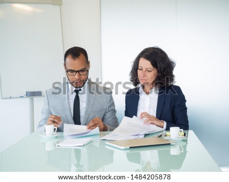 Business professionals examining contract text. Business man and woman sitting at meeting table and reading papers together. Paperwork and teamwork concept