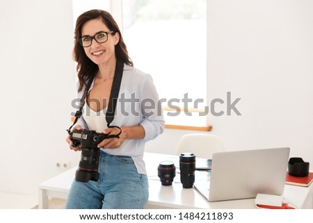 Photo of a cheery positive optimistic young photographer woman in office with camera.
