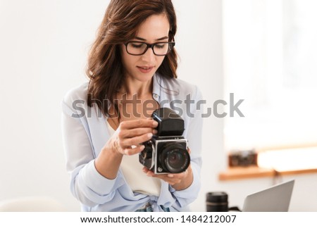 Image of amazing young pretty photographer woman in office holding retro old camera.