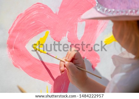 Baby girl paints with a  brush on a white wall with pink paint.