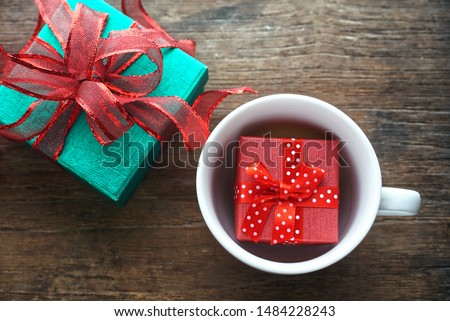 Top view small red gift box in coffee cup and green glitter gift box with red ribbon on wood table, christmas and happy new year theme.  