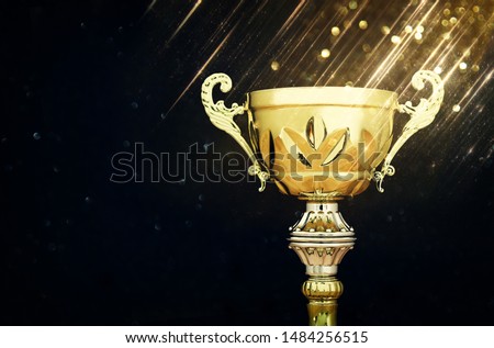 sports concept low key image of gold trophy over dark background, with abstract shiny lights