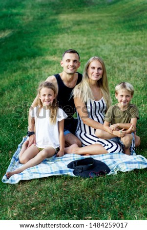 Picture of parents with children sitting on plaid on picnic on summer day