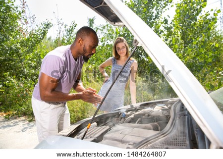 Young multiethnic couple broke down the car while traveling on the way to rest. They are trying to fix the broken by their own or should hitchhike, getting nervous. Relationship, troubles on the road