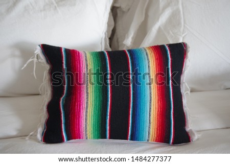 A colorful striped woven pillow on a bed setting a lively and friendly decorative accent