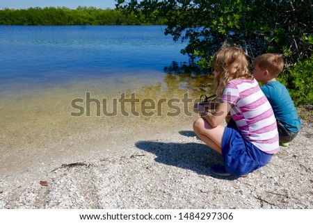 Girl and boy crouched next to a lake in J. N. Ding Darling National Wildlife Refuge, Sanibel Island, Florida Royalty-Free Stock Photo #1484297306