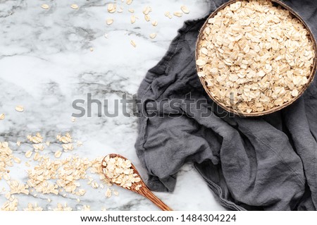Healthy raw uncooked quick oat flakes in a wooden bowl over a marble table background. Shot from top view.