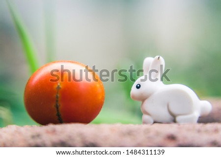 A white rabbit a toy on a stone among grass and flowers