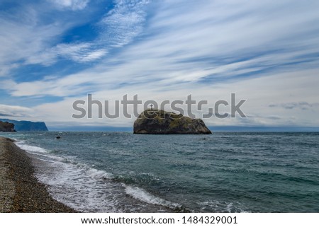 Rock with a cross stands in the sea against the cloudy sky
