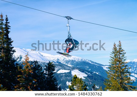 People skiers on Chair lift on Penken park ski resort in Tyrol in Mayrhofen in Zillertal valley, Austria in winter Alps. Cable cars in Alpine mountains with white snow, blue sky. Austrian snowy slopes