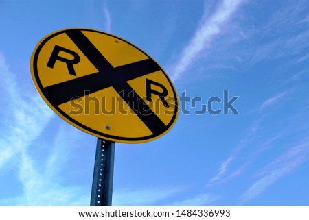 Railroad crossing sign with blue sky and clouds