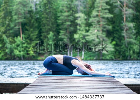 Young attractive girl practicing yoga, sitting in Child exercise, Balasana pose  on the lake. The concept of appeasement,  healthy lifestyle