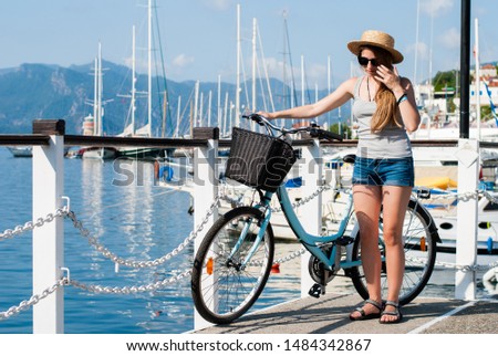 Lovely girl with retro bicycle stands on the pier in the port. Mediterranean sea and Turkish mountains in the background.