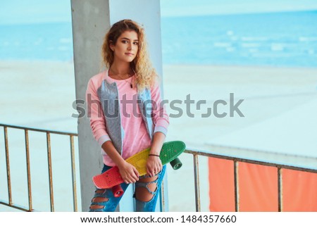 Pretty young woman is posing for photographer with skateboard near seaside.