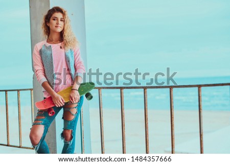 Pretty young woman is posing for photographer with skateboard near seaside.