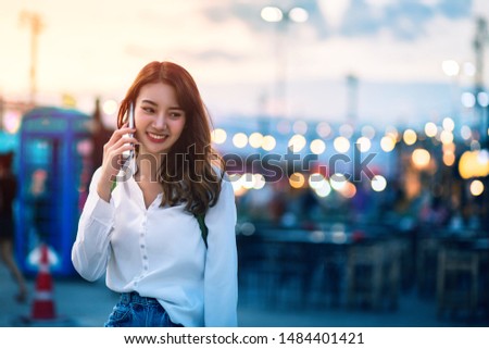 Happy young travel asian woman using smartphone and relax on street market against light bokeh background at dusk in Bangkok, Thailand, Travel vacation city concept