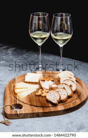 Cheese, nuts and tiny bread for brunch on a wooden plate ad white wine