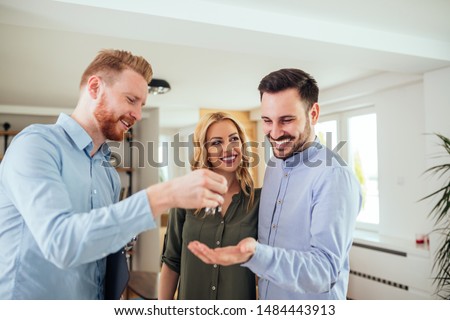 Real estate agent handing over the key to the happy couple Royalty-Free Stock Photo #1484443913