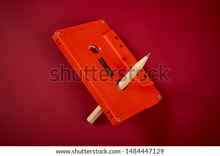 old orange audio cassette and pencil on dark red background
