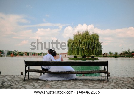 two people hugged on the bench. A picture from the back of a young couple sitting on a bench hugging. the girl lies on the groom's shoulder. Wedding photo of two in love
