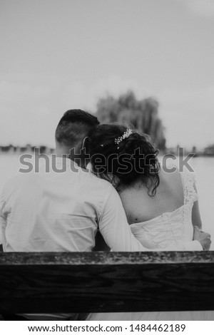 two people hugged on the bench. A picture from the back of a young couple sitting on a bench hugging. the girl lies on the groom's shoulder. Wedding photo of two in love