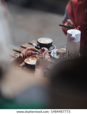 Coffee with latte art on a table with two people enjoying them and taking pictures of the coffee