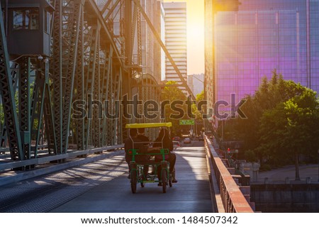 A group of people on a surrey bike in downtown Portland during a sunset with colorful buildings in the background.
