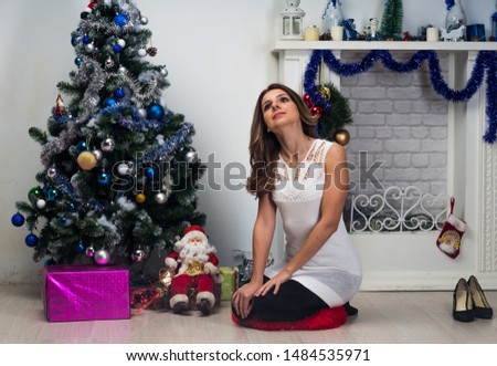 Christmas or New year celebration. Young woman in a festive white dress sits near the Christmas tree at home