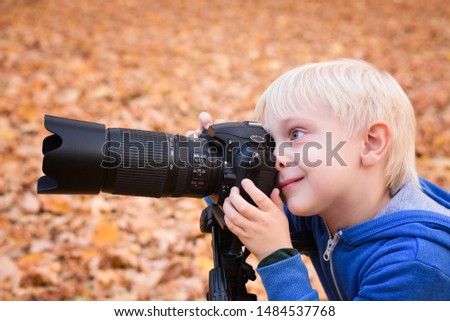 Portrait of little blond boy takes pictures on a SLR camera. Autumn Park