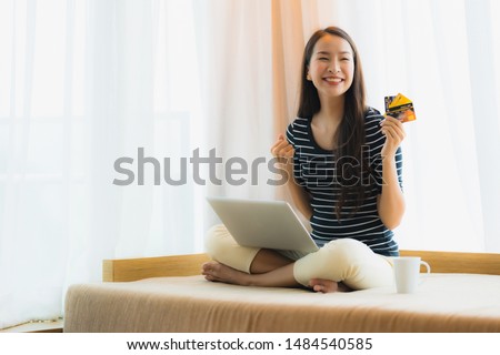 Portrait beautiful young asian woman using computer notebook or laptop with credit card for shopping on sofa in living room area
