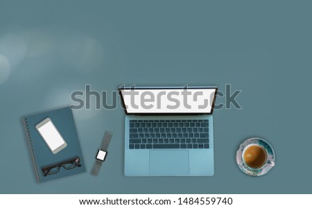 Laptop on green desktop in modern office with accessories - top view on desk from above.