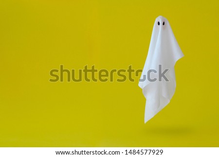 White ghost sheet costume flying in the air with yellow background. Minimal Halloween scary concept.