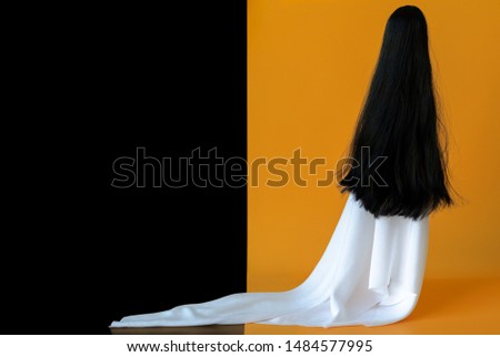 Long hair female ghost with white sheet costume with black and orange background. Minimal Halloween scary concept.