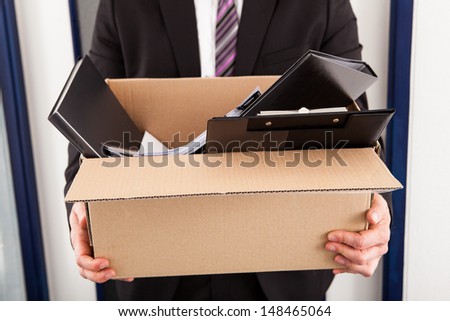 Portrait of young businessman holding cardboard in office Royalty-Free Stock Photo #148465064