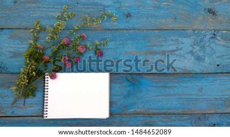 Mockup - notebook on wooden background. A sketchbook and a bouquet of clover lie on old blue boards. Flatlay for backgrounds, texts, desktops, banners, covers, postcards, to-do lists.