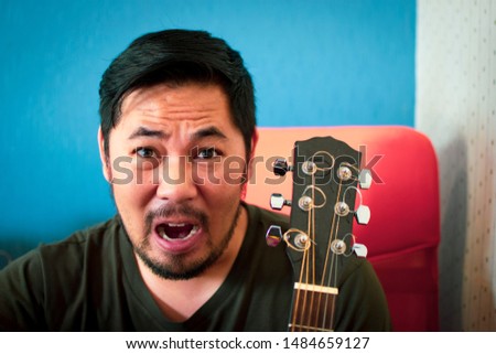 Bearded man shout and headstock of acoustic guitar with a blue and white color blurred backdrop in studio.