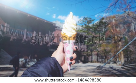 Woman's hand holding Soft white milk cream ice cream cone on light nature blue sky background