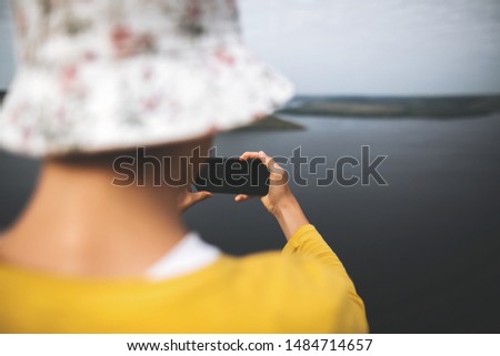 Hipster teenager streaming live while standing on top of rock mountain with amazing view on river. Young stylish guy exploring and making video of travel. Copy space