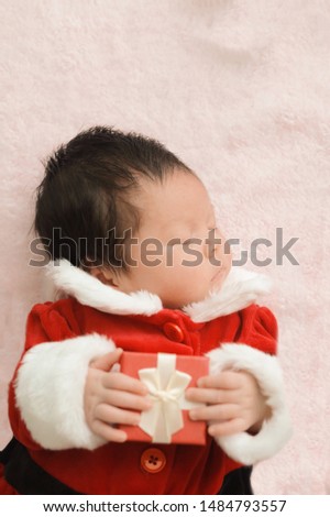 Portrait lovely newborn in red dress with gift box sleeping on mat,happy Christmas celebration time concept.